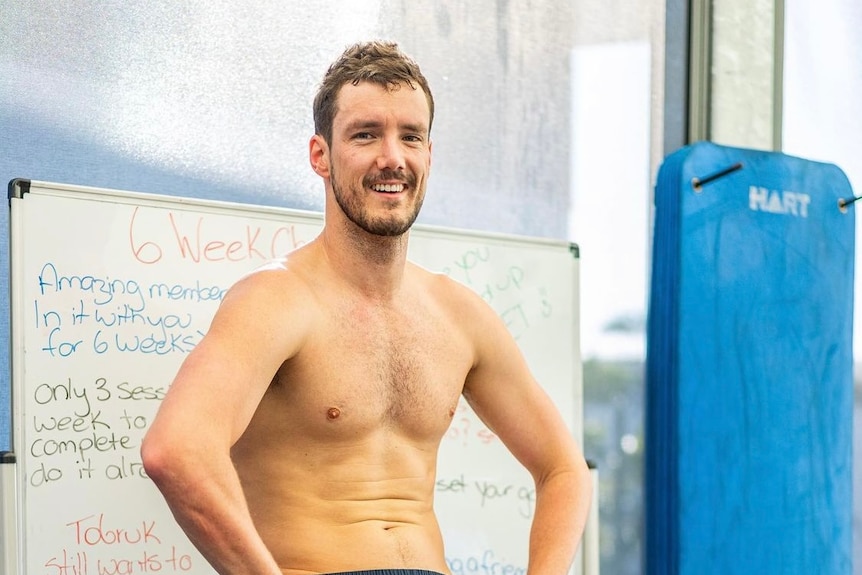 A shirtless para-athlete sits smiling in what appears to be a locker room.