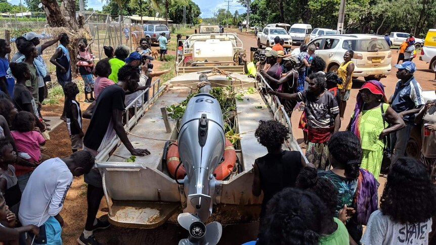 People cluster around a boat containing a trussed crocodile.