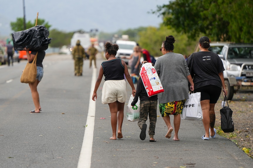 a family walks down the side of a closed highway carrying bags of belongings