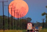 A red full moon rises over vehicles driving along a road south of Alice Springs