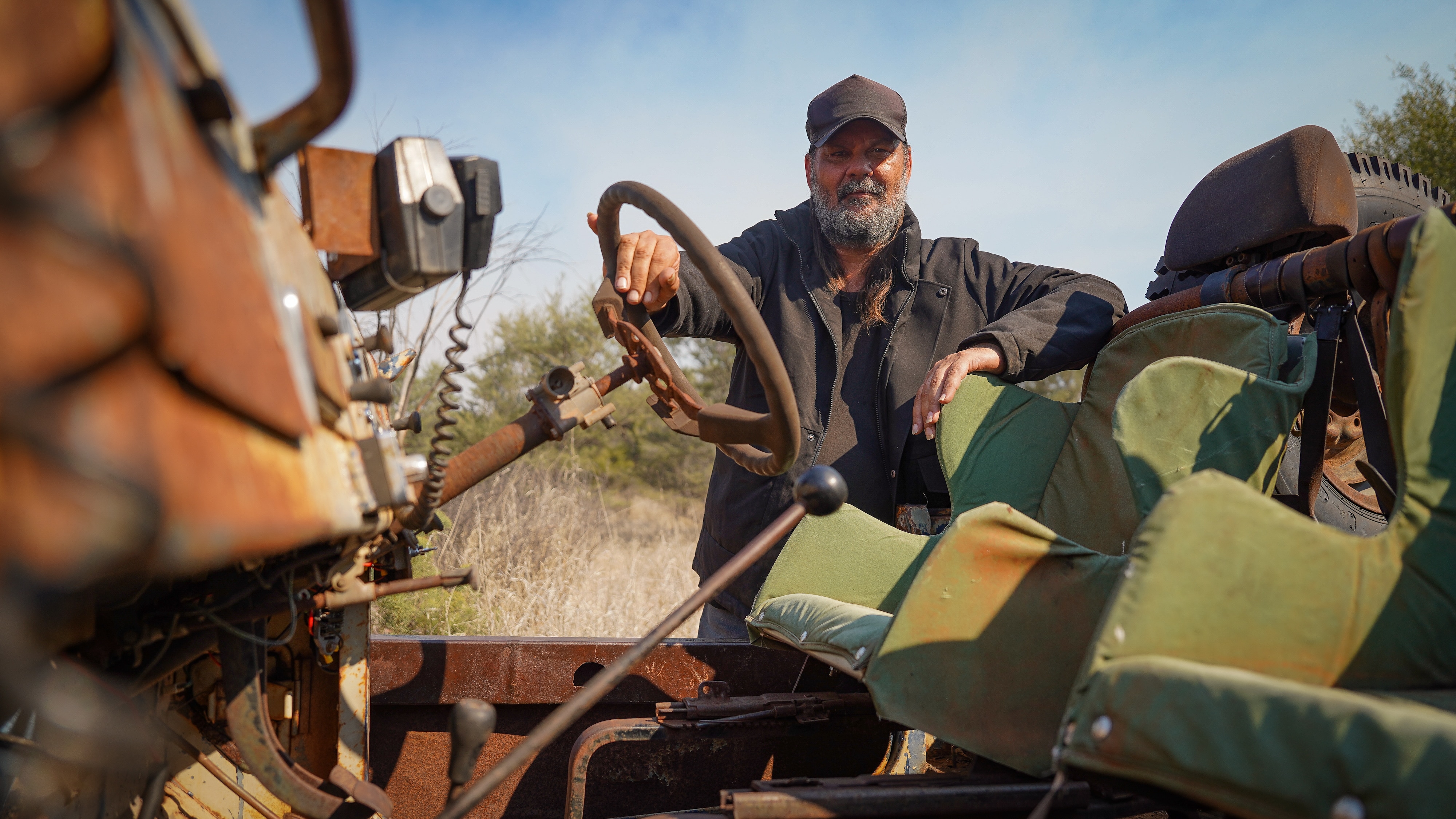 Warwick Thornton poses behind his bull catcher with his hand resting on the steering wheel.