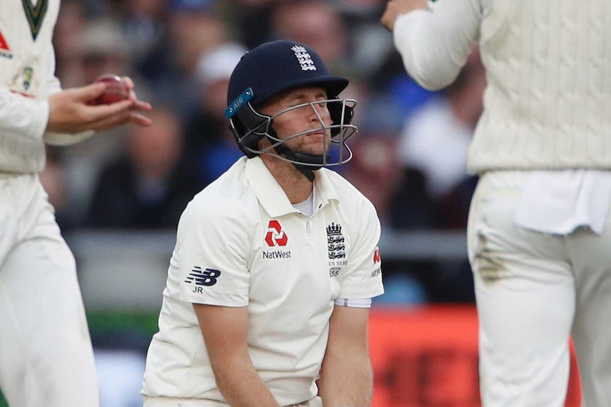 England batsman Joe Root on the ground during a Test match. Australian fielders Marcus Harris and Matthew Wade look at the ball.