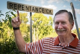 Ken Arnett stands at the side of the road with the Repentance Creek sign behind him.