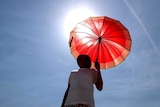 A hot weather photo of a person holding a parasol with the sun behind them