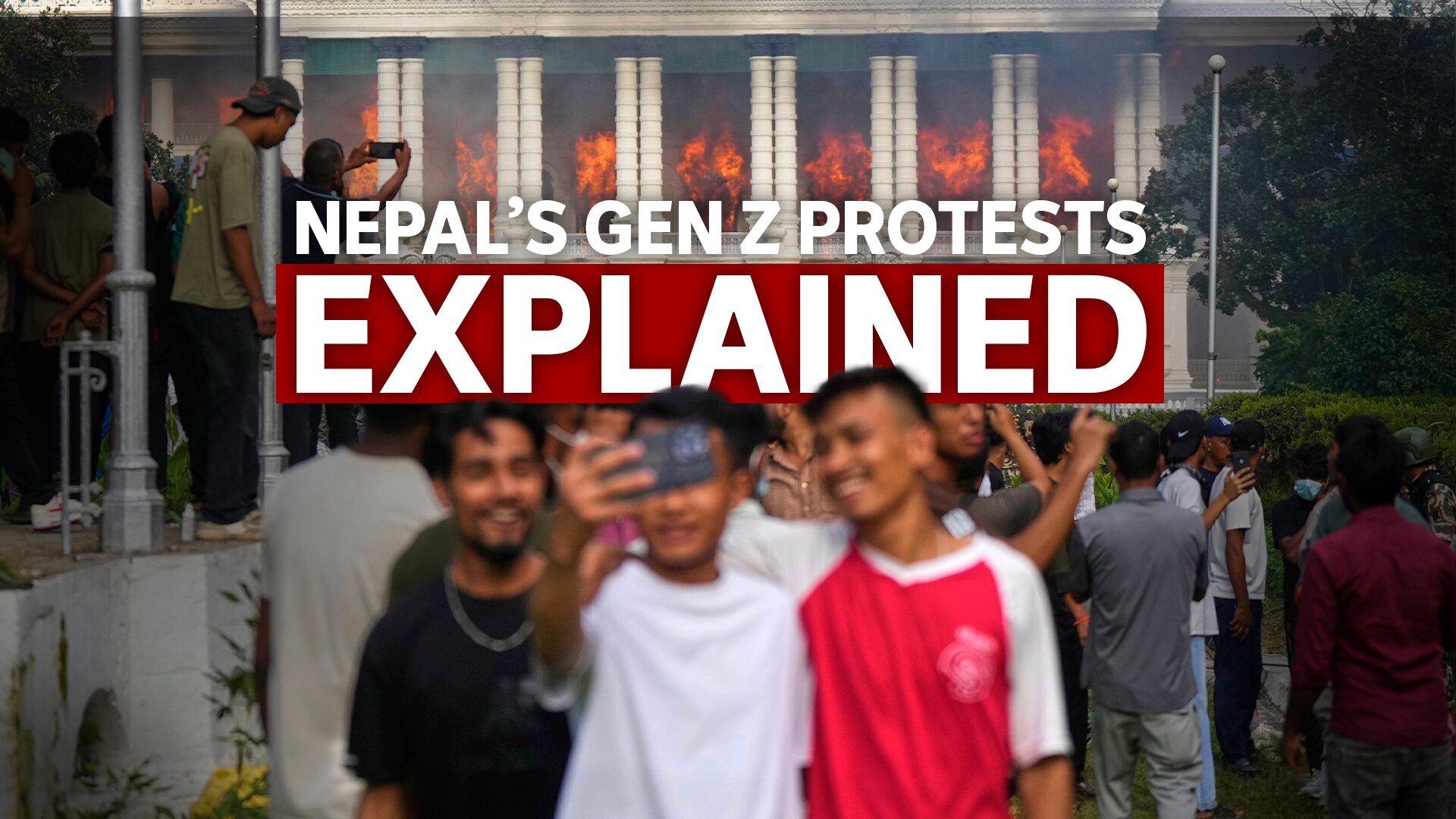 three teenagers smile for a selfie while Singha Durbar palace burns in the background.