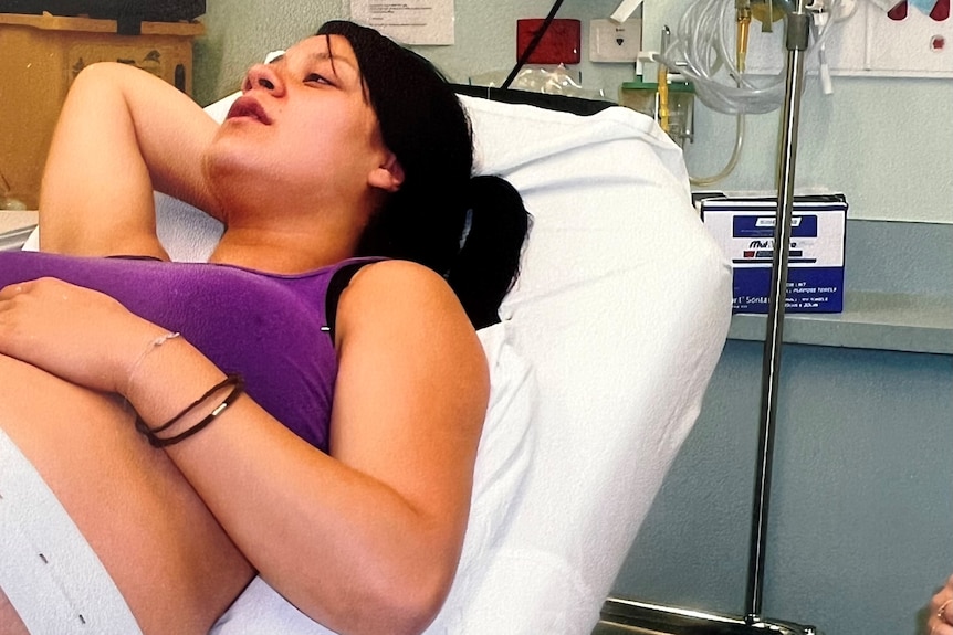 A woman lies on a hospital bed with her right hand tucked behind her head.