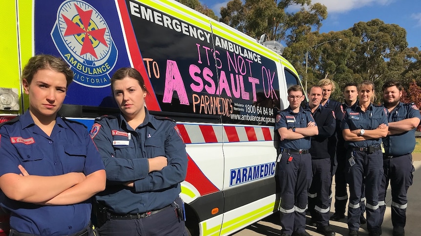 Paramedics standing in front of their vehicle with the words it's not ok to assault paramedics