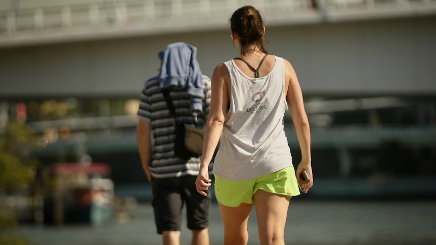 woman in gym gear walks in glaring sun along Brisbane River