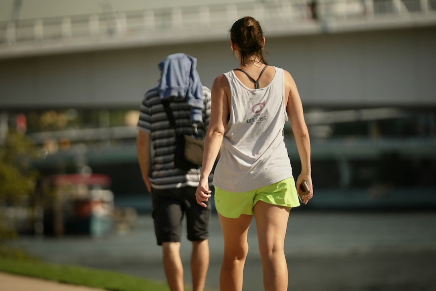 woman in gym gear walks in glaring sun along Brisbane River