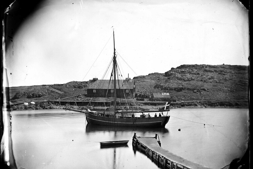 Wide black and white archive shot of a wooden ship moored in a harbour.
