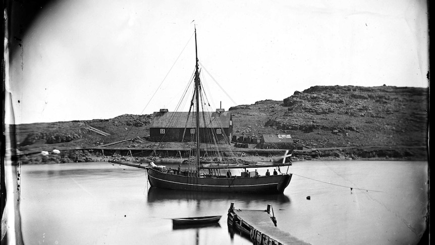 Wide black and white archive shot of a wooden ship moored in a harbour.