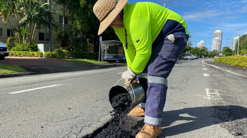 Road crew worker in high vis shirt filling a pothole with gravel from a bucket. 