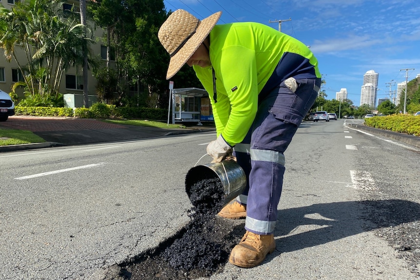 Road crew worker in high vis shirt filling a pothole with gravel from a bucket. 