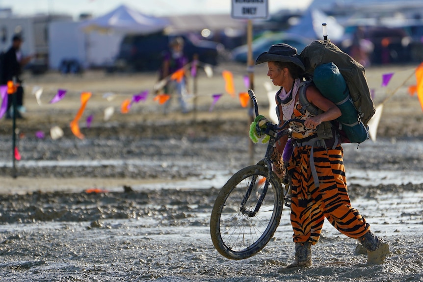 Woman in tiger print pants trudges through mud with bike 