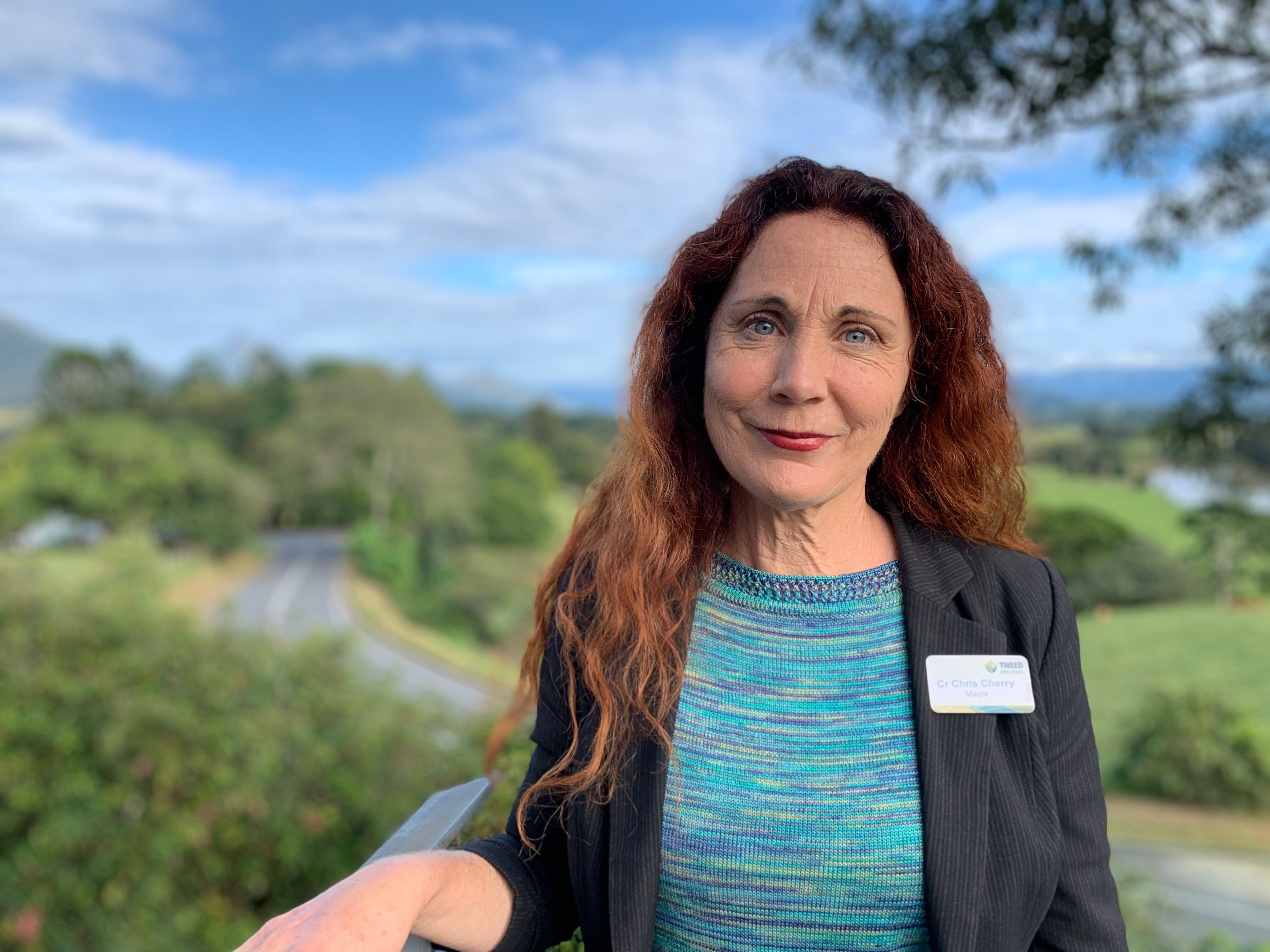 A smiling woman with river and green paddocks behind her.