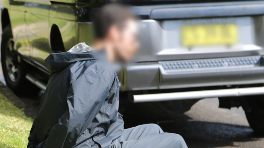 A man sits in the gutter, wearing handcuffs