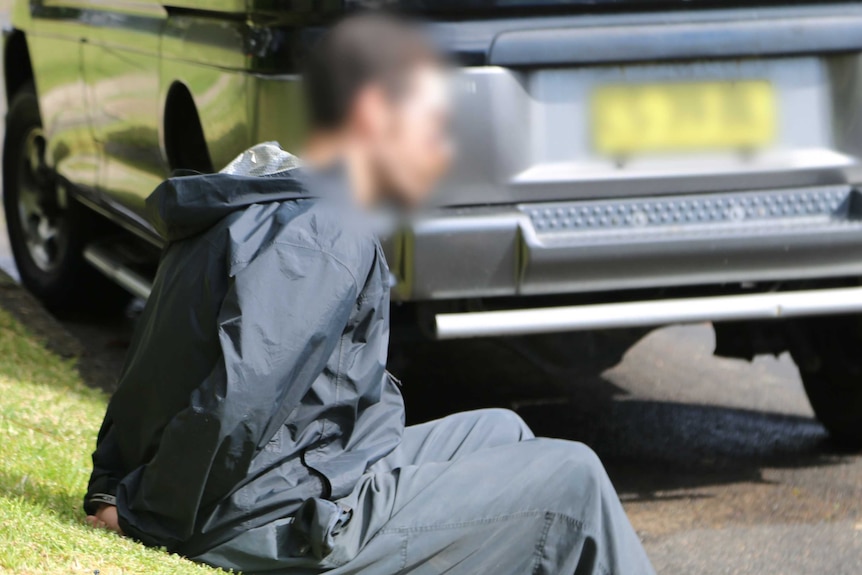 A man sits in the gutter, wearing handcuffs