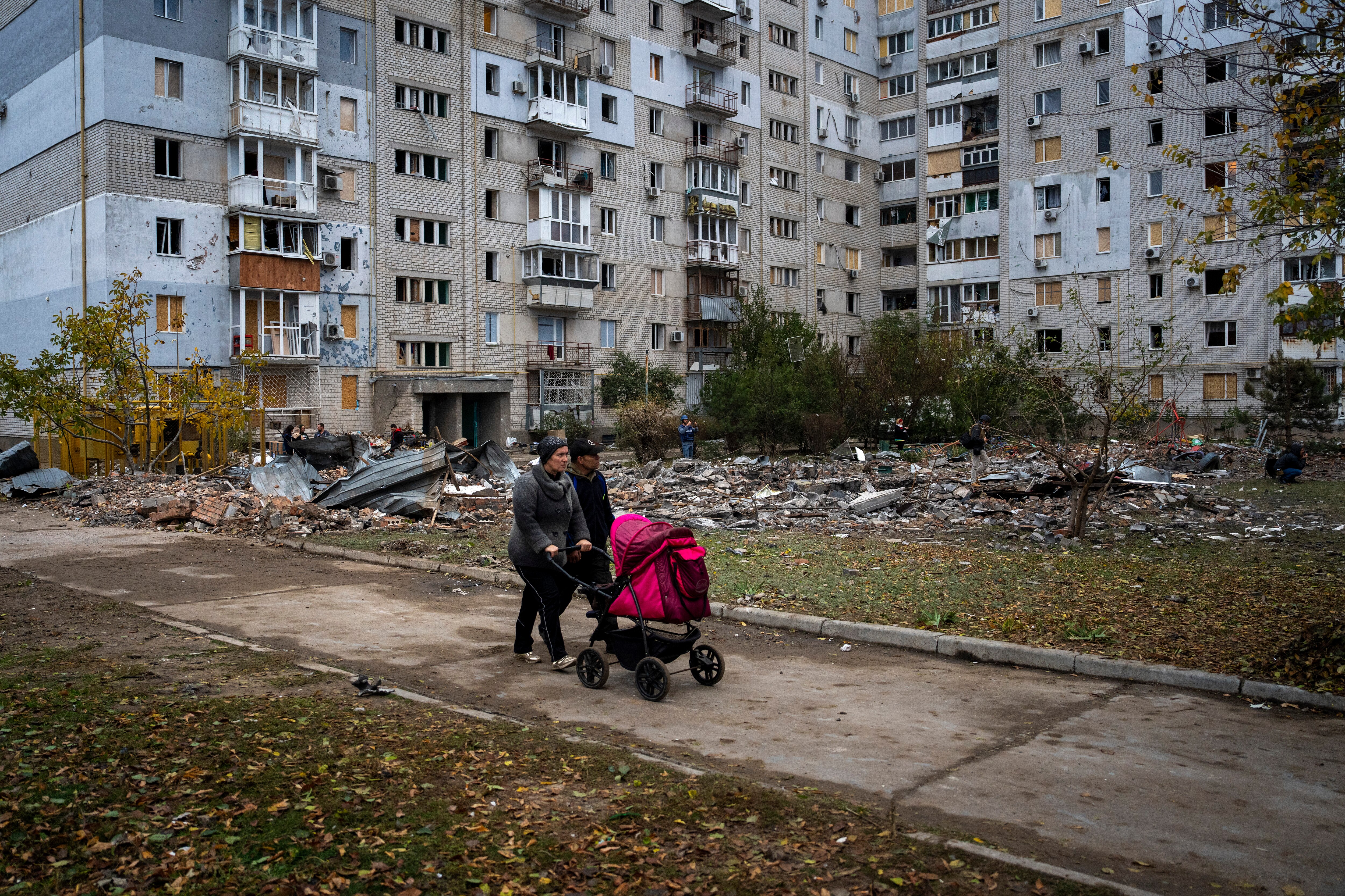 A couple pushing a baby stroller walks past a building damaged by a Russian missile.