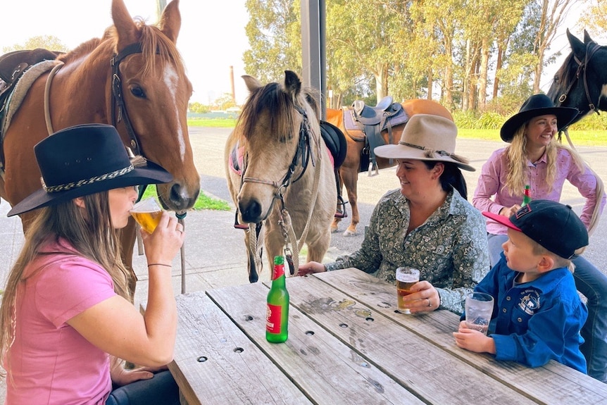 People drinking beer on a park bench in Toora, with horses in the background.