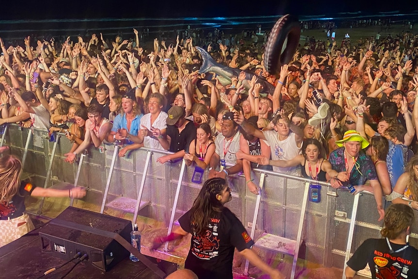 A huge group of teenagers with their arms in the air at a concert