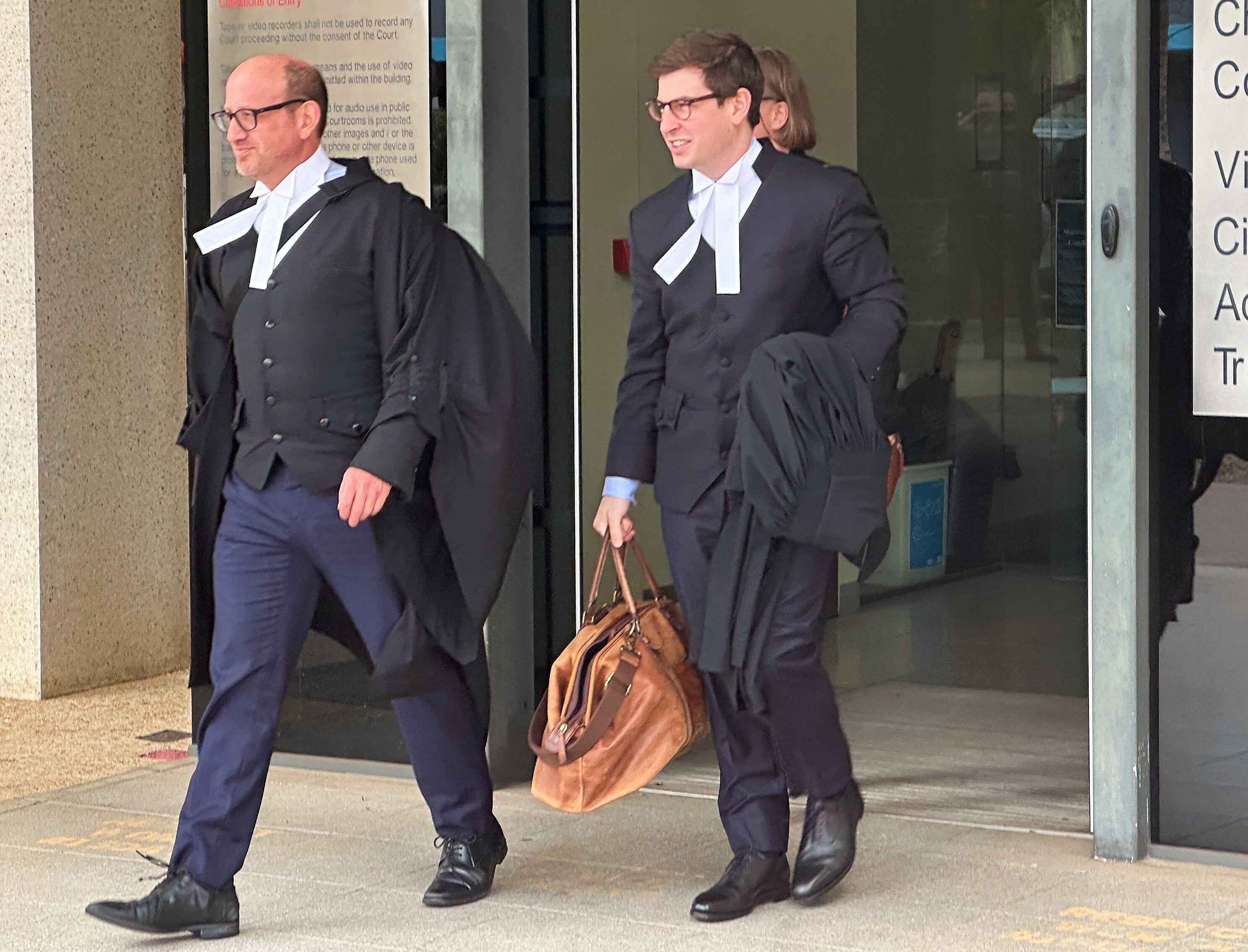 Two men in court clothing walk out a door.