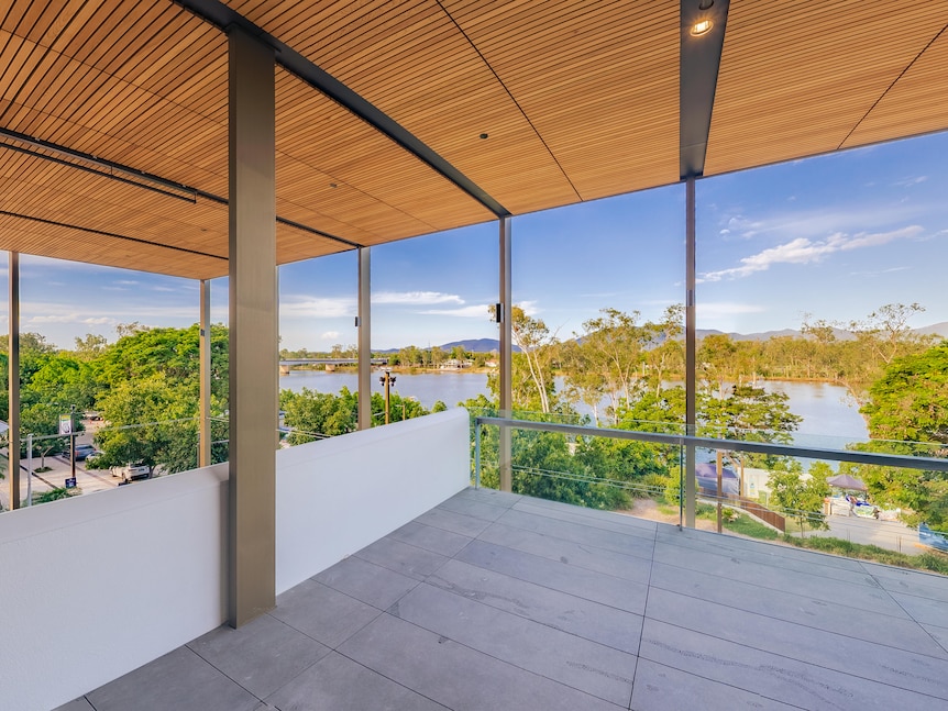 A panoramic shot from inside a gallery with glass walls, looking out onto a blue sky, trees and a river. 
