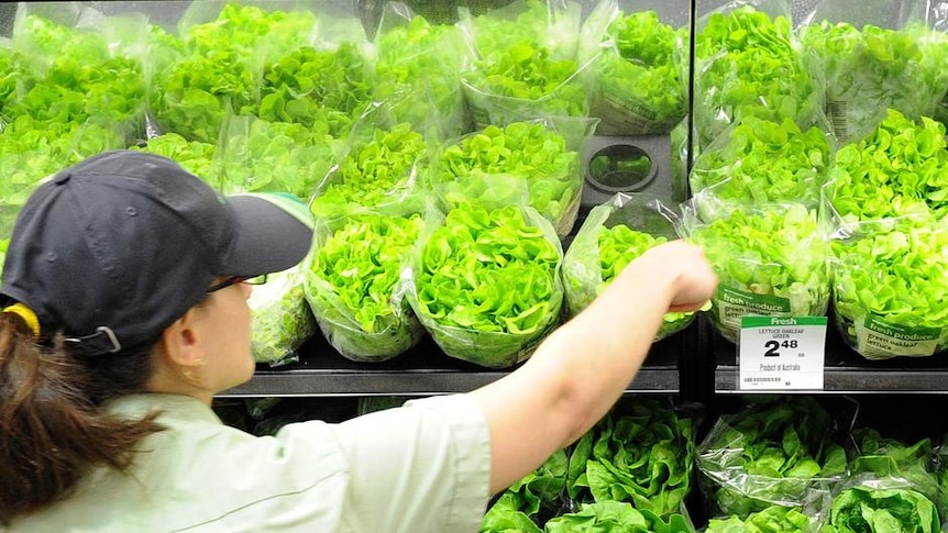 An employee arranges vegetables on display inside a supermarket