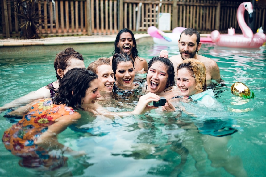 A group of people together in a swimming pool smiling for a selfie.