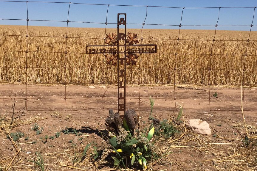 A cross sits next to a barbed wire fence.