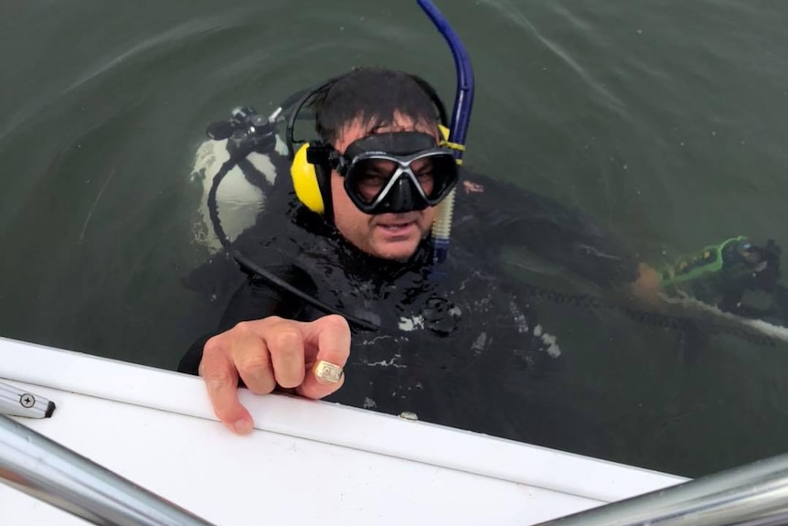 Un homme portant un équipement de plongée sous-marine dans l'eau, tenant une bague en or.