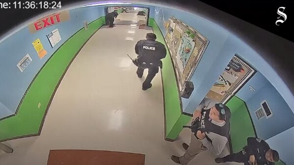 Police officers stand in a school hallway. 