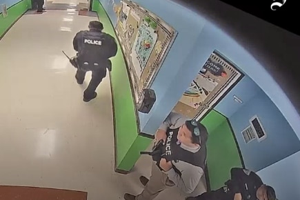 Police officers stand in a school hallway. 