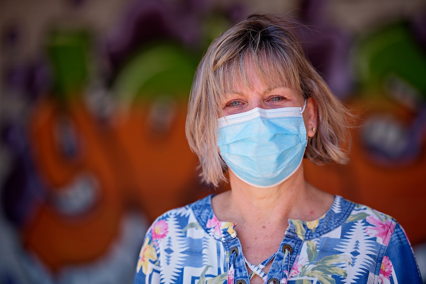 Katherine MLA Jo Hersey wearing a face mask, standing outside in front of a colourful mural.