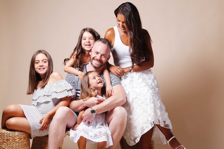 A husband and wife pose with their three daughters for a professional photo.