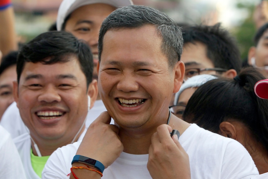 Hun Sen, wearing white T-shirt, bracelets and a watch, smiles in a crowd of people
