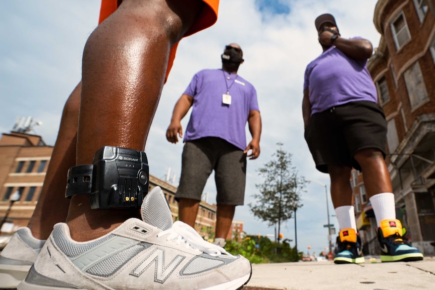 A black ankle monitoring bracelet on a man's leg