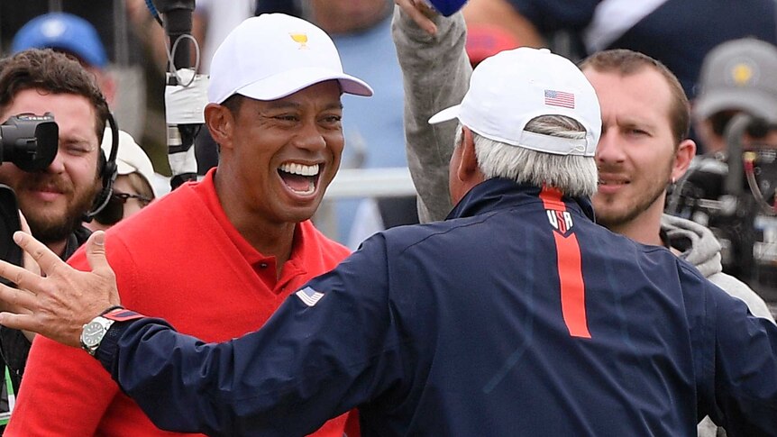 Tiger Woods smiles as Fred Couples comes in to embrace his teammate