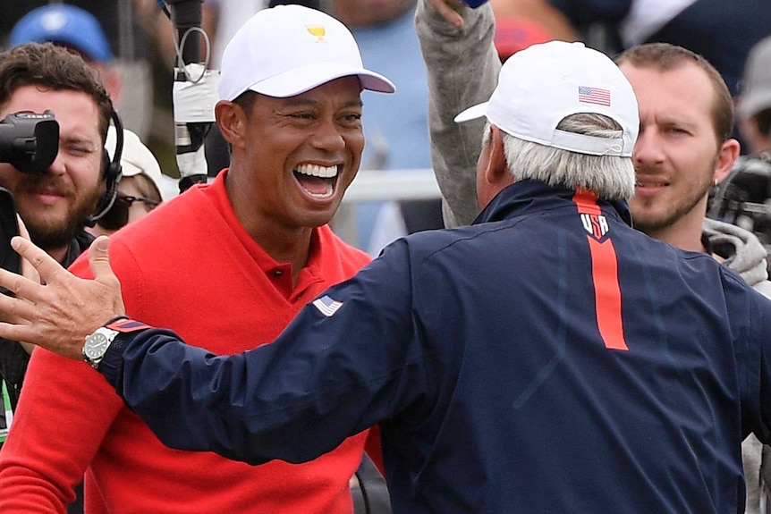 Tiger Woods smiles as Fred Couples comes in to embrace his teammate