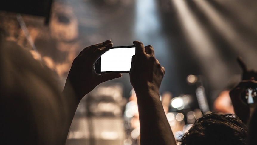 A person holds up a mobile phone to record a concert