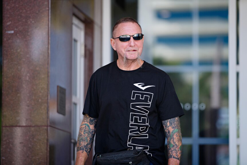 A man walks out of the NT Supreme Court wearing a black shirt. He is in his 50s with white facial hair and a serious expression.