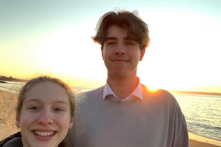 A young couple at the beach smile at the camera.