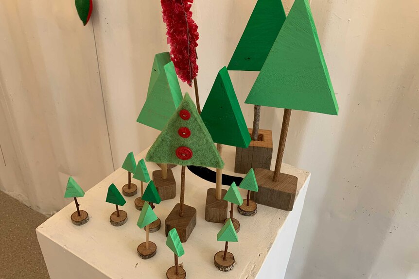 A collection of small Christmas trees made out of recycled materials on a white pedestal.