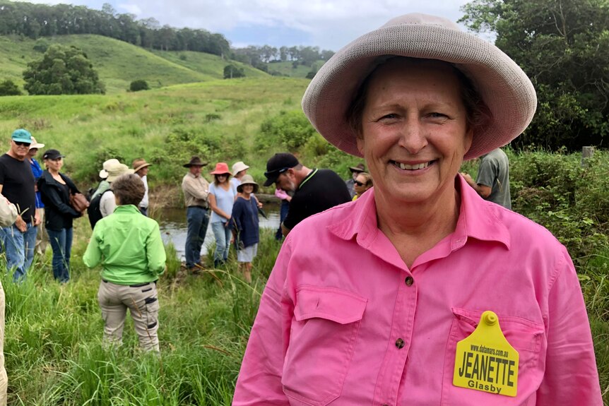 A woman in a pink shirt with a cattle ear tag name tag and a group of people behind her in a paddock.