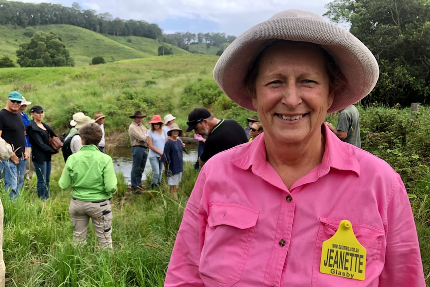 A woman in a pink shirt with a cattle ear tag name tag and a group of people behind her in a paddock.