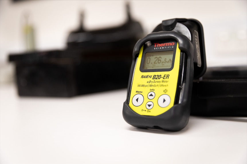 A yellow and black Geiger counter sits on an office desk.