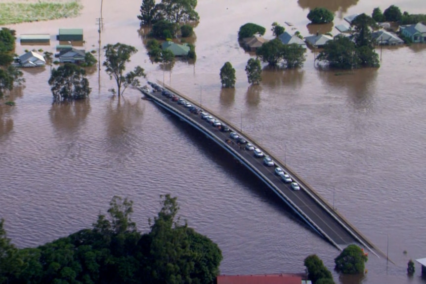 An aerial shot of cars parked on a large bridge partially flooded by an extremely swollen river.
