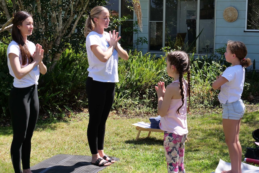 Two women lead a yoga class outside, standing in black tights, with their hands in a prayer position.