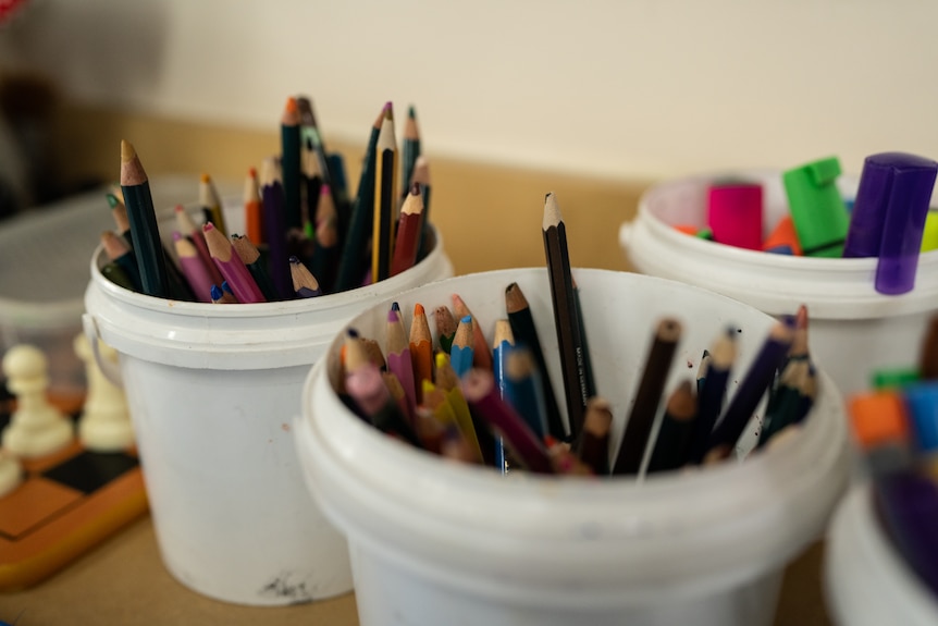 Coloured pencils and highlighters in small buckets in a school classroom.