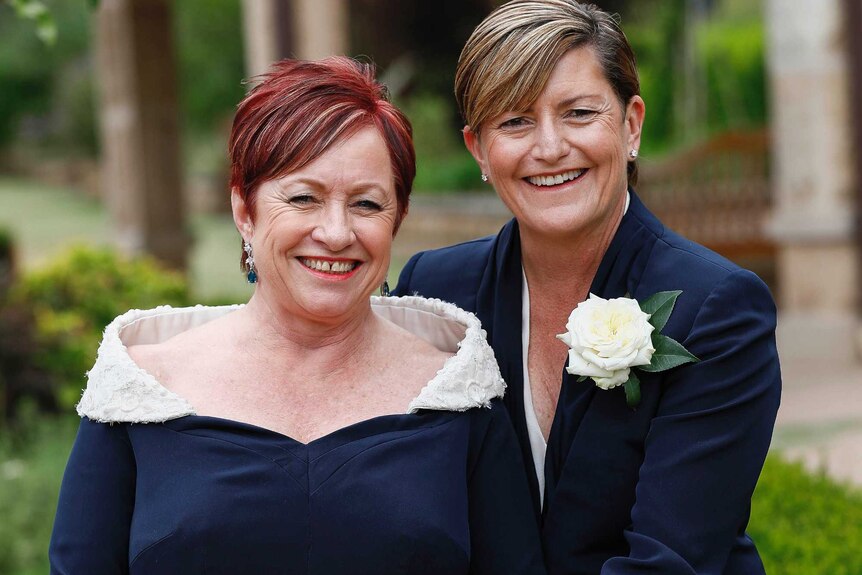 Two women in navy formal attire pose together in a garden with happy smiles