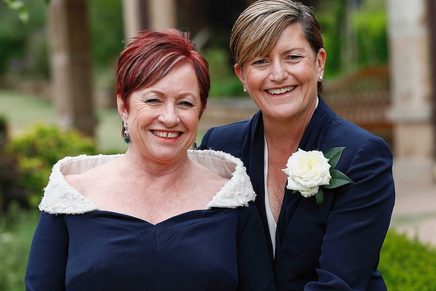 Two women in navy formal attire pose together in a garden with happy smiles